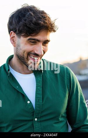 Portrait en gros plan d'un beau jeune homme avec un sourire authentique, portant une chemise verte à l'extérieur. Image capture la mode masculine moderne, attitude positive, Banque D'Images