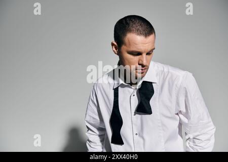 Un homme en chemise blanche et noeud papillon noir regarde vers le bas, perdu dans ses pensées. Banque D'Images