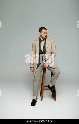 Un homme dans un costume et un manteau bronzés se penche de façon décontractée sur un tabouret en bois. Banque D'Images