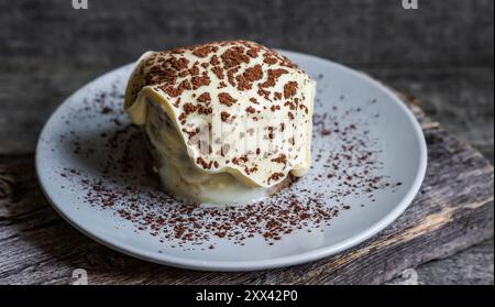 Tiramisu, dessert italien traditionnel sur assiette blanche, fond en bois. Mise au point sélective Banque D'Images