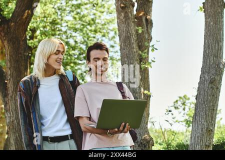 Deux jeunes amis, habillés de façon décontractée, traversent une zone boisée. L'un tient un ordinateur portable. Banque D'Images