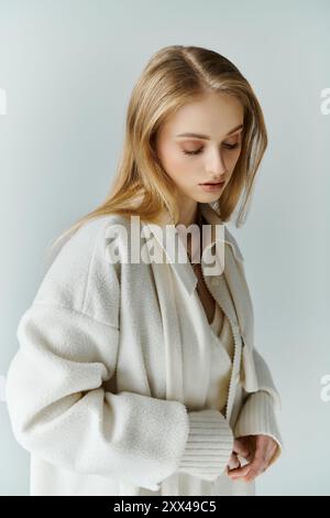 Une femme dans un cardigan blanc regarde vers le bas, ajustant ses manches. Banque D'Images
