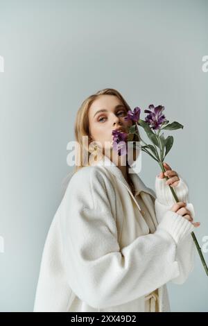 Une femme en manteau blanc tient une seule branche de fleurs de lilas sur son visage. Banque D'Images