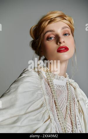 Une jeune femme dans une blouse en dentelle blanche avec les cheveux blonds, rouge à lèvres rouge et un collier de perles pose. Banque D'Images