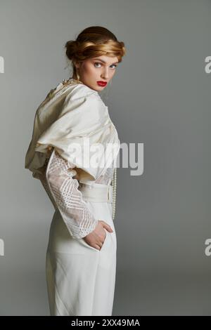 Une jeune femme dans un ensemble blanc et élégant pose sur un fond gris. Banque D'Images