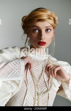 Une jeune femme ajuste un collier de perles tout en portant une élégante blouse blanche. Banque D'Images