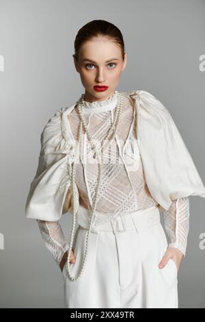 Une jeune femme pose dans un haut en dentelle blanche avec des colliers de perles et un pantalon blanc assorti. Banque D'Images