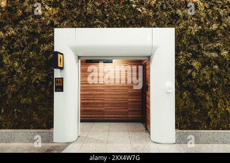 Entrée aux toilettes pour femmes au design moderne, avec un portail blanc, des murs en bois et un jardin vertical sur le côté. Lumineux, propre et accède Banque D'Images