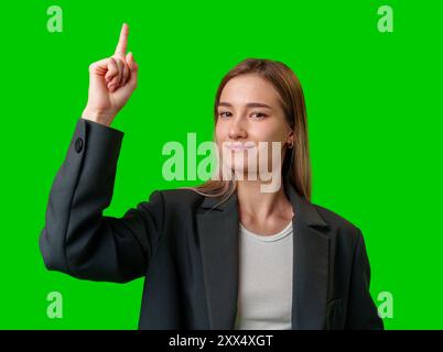 Jeune femme en Blazer noir pointe vers le haut contre l'écran vert Banque D'Images