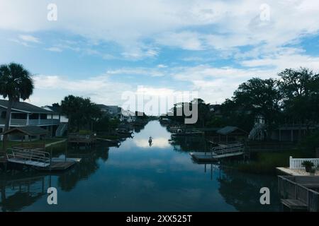 Deux personnages dans un canoë pagaie devant de vieux quais sous un ciel bleu avec des nuages dans un canal en bord de mer sur la côte de Caroline du Sud. Banque D'Images