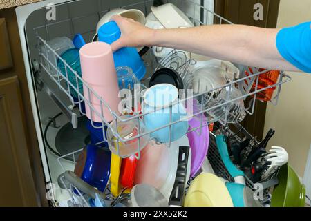 Gros plan horizontal de la main d’une femme mettant un gobelet en plastique dans le lave-vaisselle. Banque D'Images