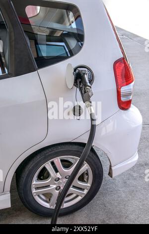 Gros plan vertical d'une petite voiture blanche obtenant de l'essence à partir d'une buse à essence. Banque D'Images