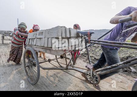 Après le séchage des briques d'argile brute, elles sont empilées à l'intérieur d'un four de briques à cheminée fixe le long de la rivière hazy Turag à Asulia au Bangladesh. La zone est remplie de fours de briques à cheminée fixe, qui viennent de transformer leur production en grande vitesse. Pendant la plus grande partie de l'année, les fours en briques sont inondés car ils sont situés sur les lits de la rivière. Lorsque l'eau recule pendant la saison sèche, les fours reviennent à la vie alors que des centaines d'ouvriers empilent des briques fraîchement pressées en silt dans d'énormes fours à bois et à charbon. En utilisant une technique simple qui remonte des centaines d'années, la cheminée fixe bric Banque D'Images