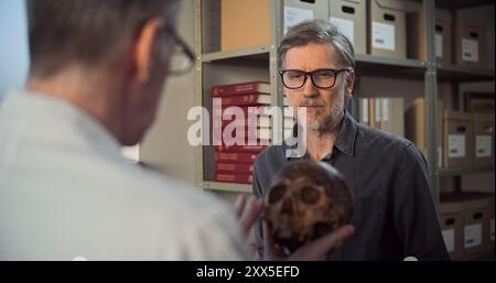 Deux archéologues analysent et examinent le crâne de l'homme éteint antique, ont des discussions au cours de recherches historiques et scientifiques sur les restes fossiles. Les scientifiques travaillent dans un laboratoire archéologique moderne. Banque D'Images