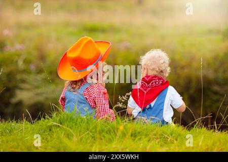 Petit garçon et fille habillés comme cow-boy et cow-girl jouant avec jouet cheval à bascule dans le parc. Les enfants jouent à l'extérieur. Enfants en costumes d'Halloween Banque D'Images