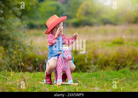 Petit garçon et fille habillés comme cow-boy et cow-girl jouant avec jouet cheval à bascule dans le parc. Les enfants jouent à l'extérieur. Enfants en costumes d'Halloween Banque D'Images