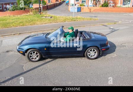 Une personne conduit une voiture de sport décapotable vert foncé dans une rue résidentielle par une journée ensoleillée. Banque D'Images