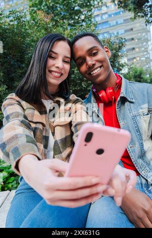 Vertical. Jeune couple multiracial aime naviguer sur Internet sur un téléphone portable. Deux amis adolescents utilisent un smartphone pour partager du contenu sur une application de médias sociaux. Les jeunes regardent l'écran du téléphone portable. Photo de haute qualité Banque D'Images