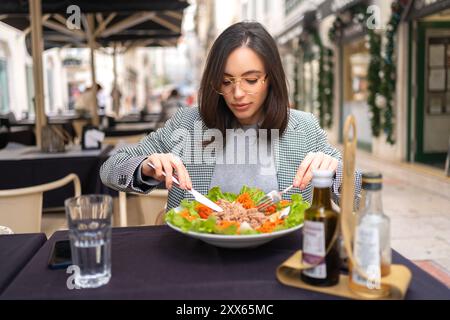 Femme d'affaires élégante mangeant une salade saine sur la terrasse du restaurant, se sentant heureuse le jour d'été Banque D'Images
