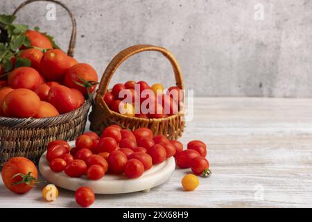 Tomates fraîches grandes et petites dans des paniers et sur un plateau blanc sur une table en bois Banque D'Images