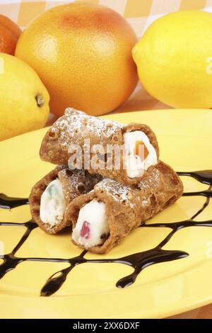 Gros plan de mini cannoli siciliens originaux sur une plaque jaune. Ces pâtisseries en forme de tube sont faites de coquilles frites remplies d'un mélange sucré de riques Banque D'Images