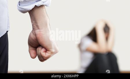 Violence familiale et concept d'agression, homme furieux en colère levé le poing de punition sur la femme effrayée ou terrifiée assise au coin du mur Banque D'Images