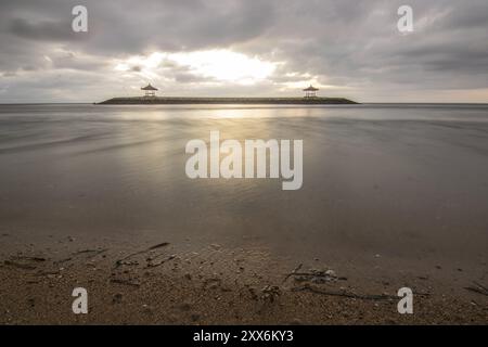 Beau paysage marin le matin. Plage de sable tropical avec brise-lames et reflet du ciel dans l'eau calme. Paysage matinal, pris à Sanur Banque D'Images