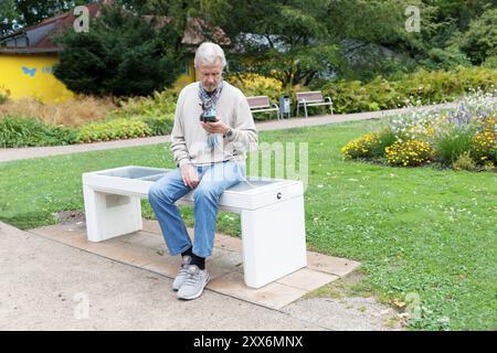 L'homme est assis sur un Smart Bench et charge son téléphone portable, banc avec option de charge Banque D'Images