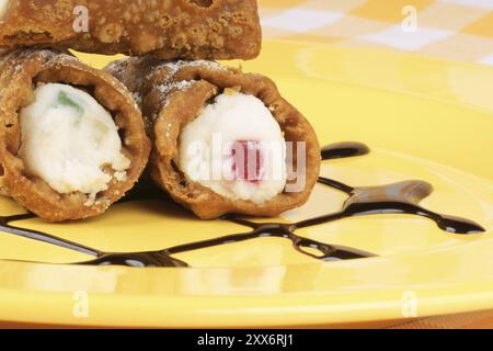 Gros plan de mini cannoli siciliens originaux sur une plaque jaune. Ces pâtisseries en forme de tube sont faites de coquilles frites remplies d'un mélange sucré de riques Banque D'Images