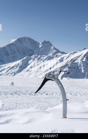 Gros plan d'une hache glacée dans la neige avec des montagnes enneigées en arrière-plan Banque D'Images