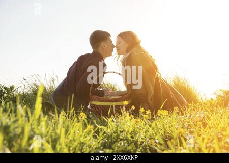 Vue de l'arrière. Jeune couple marié embrassant sur pique-nique dans la nature sur fond de coucher de soleil. Le concept d'une jeune famille heureuse et l'unité avec la nature Banque D'Images