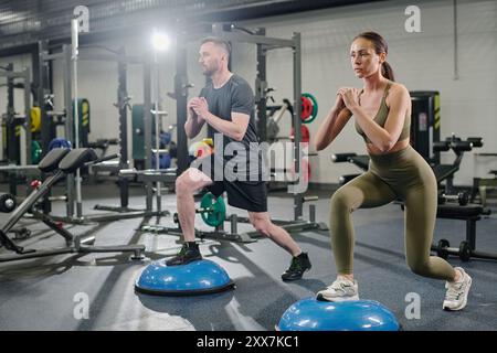 Partenaires faisant des fentes sur demi-balle ensemble dans une salle de gym moderne Banque D'Images