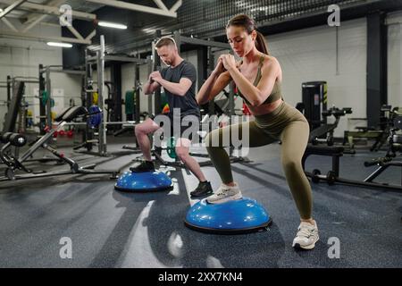 Homme et femme caucasiens pratiquant HIIT sur la formation de demi-balle bleue ensemble Banque D'Images