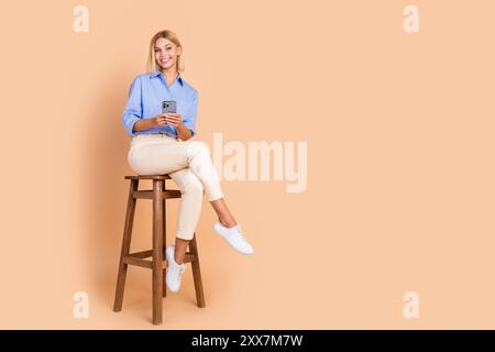 Photo pleine longueur de charmante femme positive porter une chemise bleue lisant un dispositif moderne vide espace blanc isolé fond de couleur beige Banque D'Images