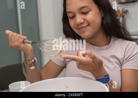 Une adolescente s'amusant à goûter la recette maison pour la boulangerie. Banque D'Images