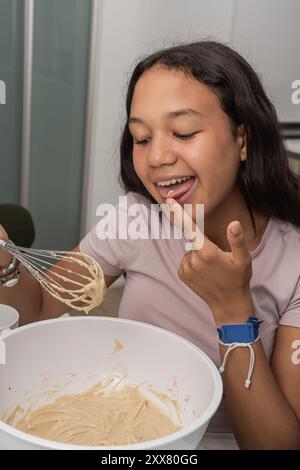 Heureux adolescent dégustant la pâte à biscuits du bol à mélanger. Banque D'Images