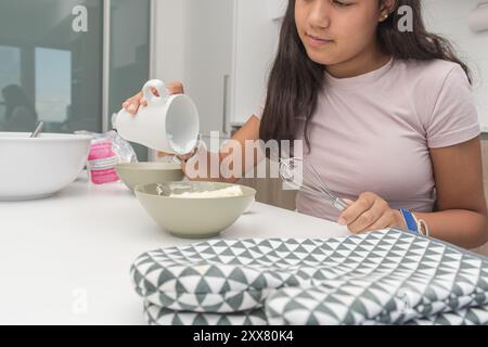 Jeune fille ajoutant de la farine au bol à mélanger tout en préparant des biscuits. Banque D'Images