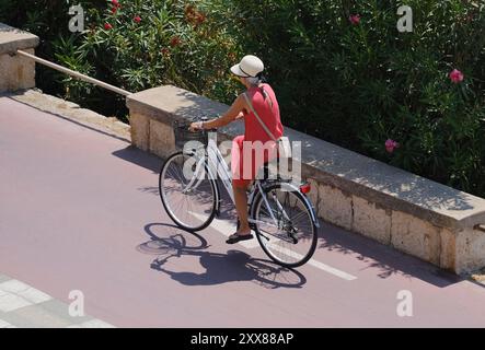 Italie, Sicile, mer Méditerranée, Marina di Ragusa (Province de Raguse), 23 août 2024, femme en vélo sur la route du front de mer - ÉDITORIAL Banque D'Images