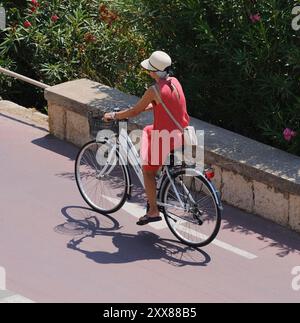 Italie, Sicile, mer Méditerranée, Marina di Ragusa (Province de Raguse), 23 août 2024, femme en vélo sur la route du front de mer - ÉDITORIAL Banque D'Images