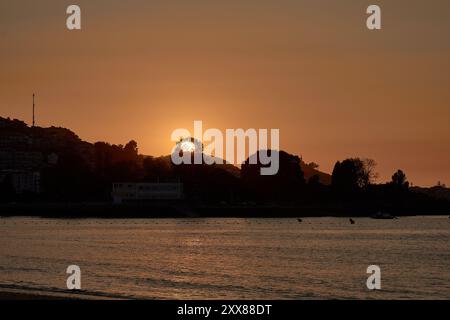 Coucher de soleil unique sur la plage de Ladeira, où le soleil se couche derrière un arbre solitaire, créant une silhouette saisissante dans le ciel du soir Banque D'Images