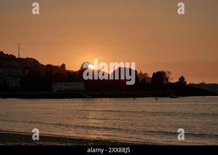 Coucher de soleil unique sur la plage de Ladeira, où le soleil se couche derrière un arbre solitaire, créant une silhouette saisissante dans le ciel du soir Banque D'Images