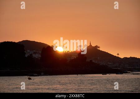 Coucher de soleil unique sur la plage de Ladeira, où le soleil se couche derrière un arbre solitaire, créant une silhouette saisissante dans le ciel du soir Banque D'Images