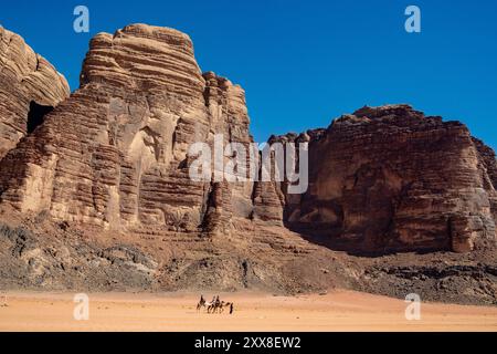 Jordanie, désert du Wadi Rum, classé au Patrimoine mondial de l'UNESCO, touristes à dos de chameaux avec leur guide bédouin devant les falaises de grès Banque D'Images