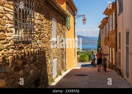 France, Var, Gassin, labellisés les plus beaux villages de France, ruelle dans le village avec deux cyclistes, le Golfe de Saint-Tropez en arrière-plan Banque D'Images