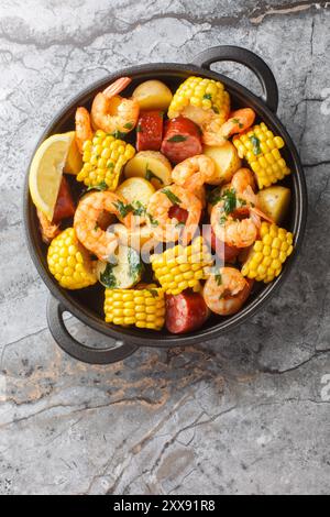 Crevettes Cajun traditionnelles bouillir avec saucisse maïs pomme de terre et citrons gros plan sur la table. Vue de dessus verticale Banque D'Images