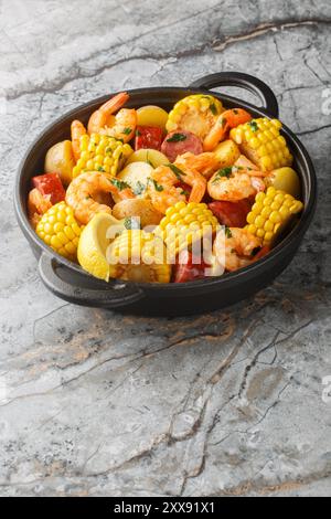 Plat du sud qui comprend des crevettes tendres, des pommes de terre copieuses, des saucisses savoureuses et du maïs sucré tous bouillis ensemble dans un gros pot en gros plan sur la table. Banque D'Images