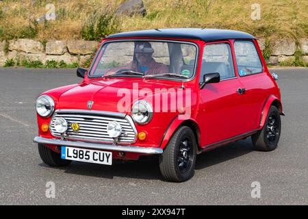 Classic Red Mini Cooper garé sur une route avec de la verdure en arrière-plan. Banque D'Images