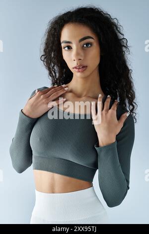 Une jeune femme dans un haut de crop top gris pose sur un fond blanc. Banque D'Images