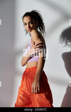 Une femme afro-américaine élégante pose dans un studio avec un fond gris, mettant en valeur sa tenue tendance. Banque D'Images