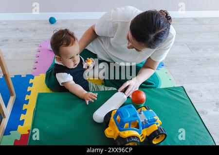 Mignon petit garçon avec des troubles neurodéveloppementaux s'engage dans la thérapie avec un gardien, en utilisant des jouets pour améliorer sa réadaptation physique et le ski à moteur Banque D'Images